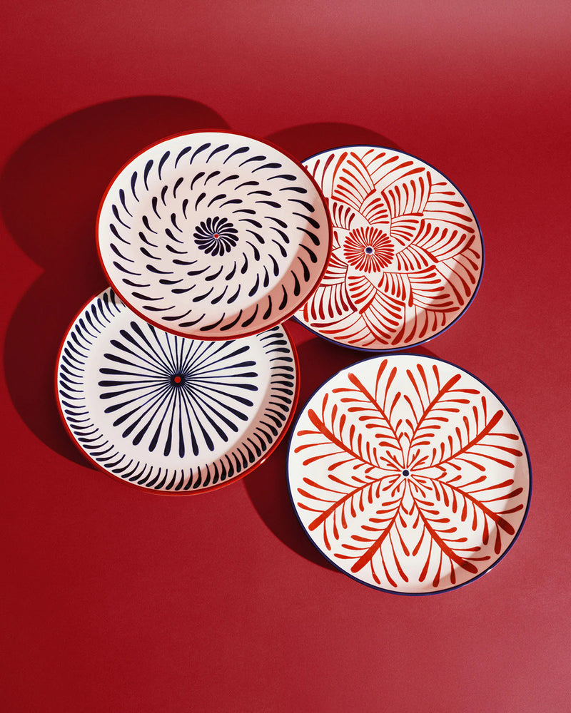 Set de 4 platos llanos con flores geométricas en rojo y azul, vista superior.