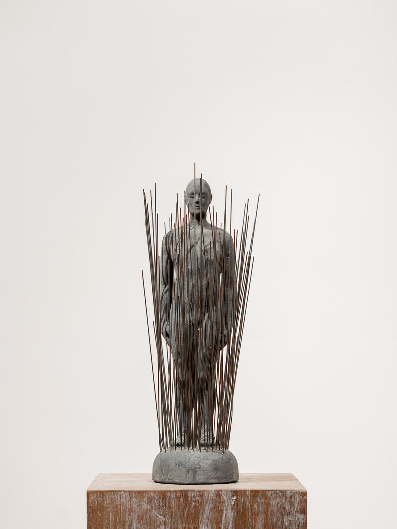 Escultura de busto con varillas metálicas verticales sobre base de piedra, gris oscuro