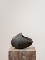 Escultura de cerámica gris oscuro con cavidad interior sobre base de madera