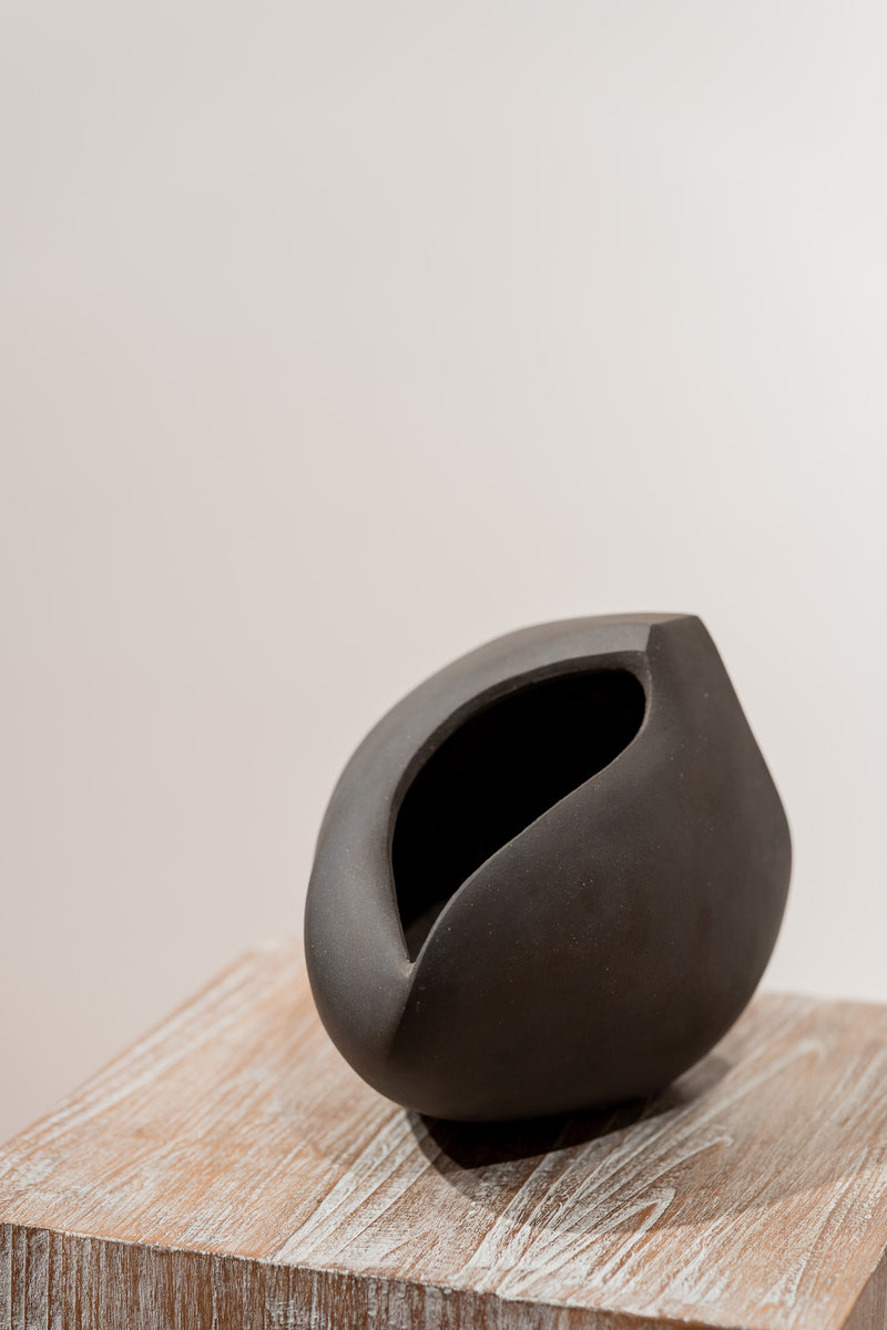 Escultura de cerámica gris oscuro con abertura superior sobre base de madera rectangular