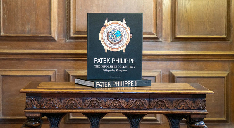 Libro con reloj y texto PATEK PHILIPPE sobre mesa de madera