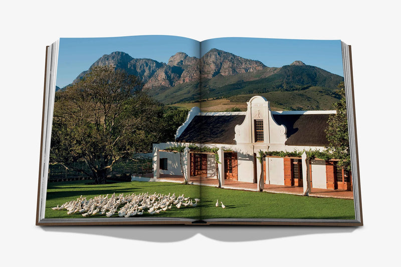 Libro abierto con foto exterior: edificio blanco con arcos, jardín y montañas al fondo.