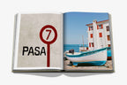 Libro Biarritz Vasca abierto; rótulo PASA en pared y foto de barco junto al mar.
