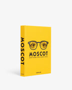 Libro con lomo y portada lateral amarilla; logotipo MOSCOT y gafas impresas