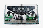Libro abierto con foto de mural oscuro y personas frente a vehículos verdes.
