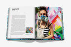 Libro abierto con foto de artista con mascarilla de respiración y mural geométrico.