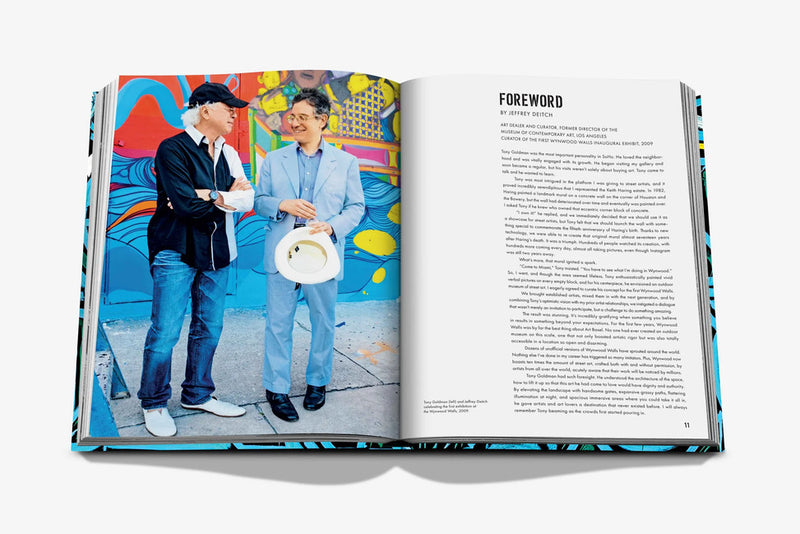 Libro abierto con foto de dos hombres conversando junto a un mural vibrante.