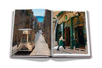 Libro abierto: calle estrecha con edificios y, a la derecha, puerta verde con arco.