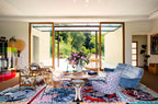 Sala con ventanales, sofá azul y alfombra geométrica con mesa y flores