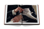 Libro abierto con foto de gato blanco sujeto por una persona con anillo