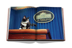 Libro abierto con gato tricolor en podio y letrero circular «The White House»