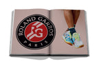Libro de Assouline abierto, logotipo y zapatillas de deporte en primer plano.