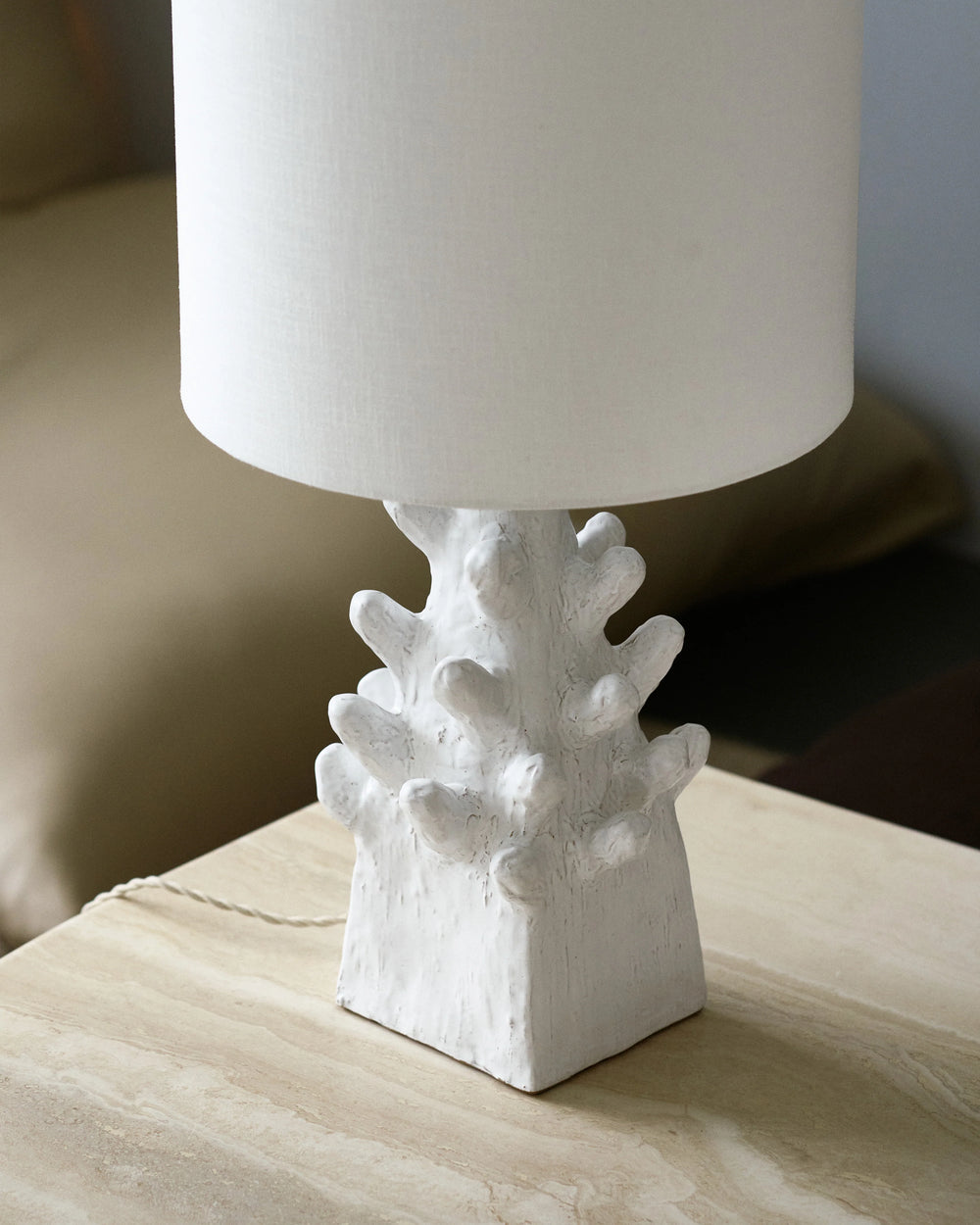 Lámpara de mesa con pantalla blanca de tela y base escultórica blanca en mesa