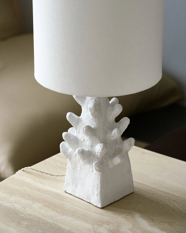 Lámpara de mesa con pantalla blanca de tela y base escultórica blanca en mesa