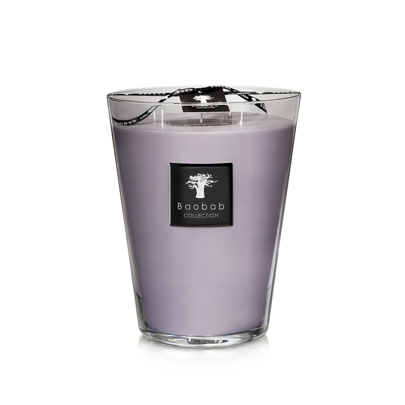 Vela en vaso de vidrio con cera morada y etiqueta negra con logotipo