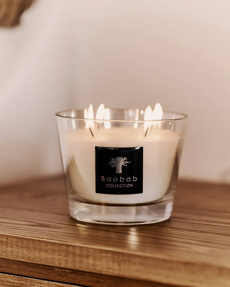 Vela en frasco de vidrio con cera blanca y etiqueta Baobab Collection, llamas visibles