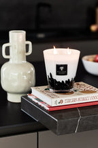 Vela blanca en vaso con llama encendida y etiqueta Baobab Collection sobre libros