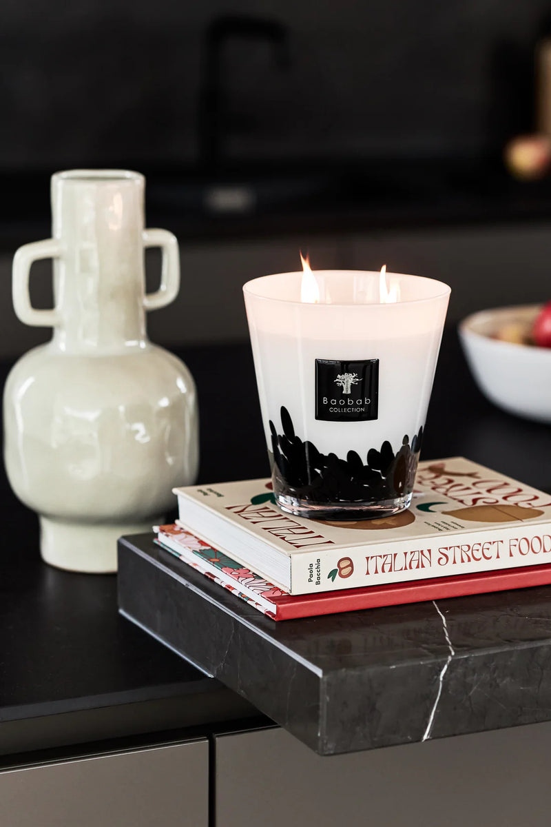 Vela blanca en vaso con llama encendida y etiqueta Baobab Collection sobre libros