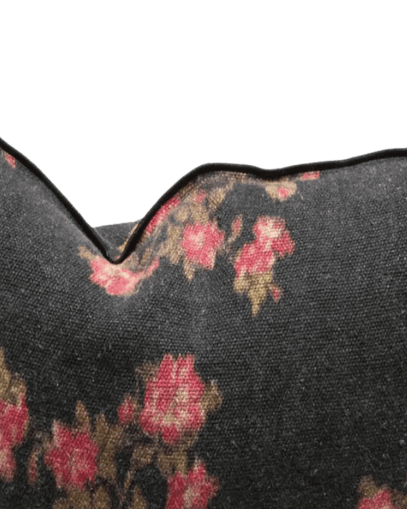 Cojín negro con estampado floral rosado, costura y borde ondulado en primer plano