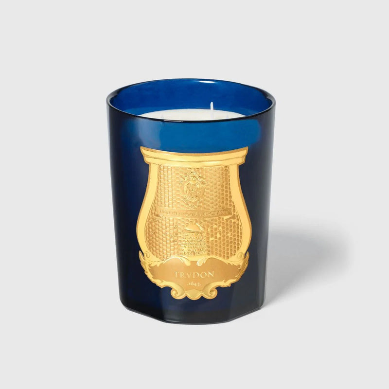 Vela en vaso de vidrio azul con motivo dorado y mecha visible