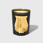 Vela en recipiente de vidrio negro con etiqueta dorada y cera blanca visible