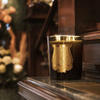 Vela en vaso de vidrio negro con emblema dorado, llama encendida